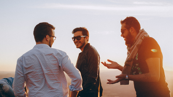 Three men laughing together outdoors at sunset
