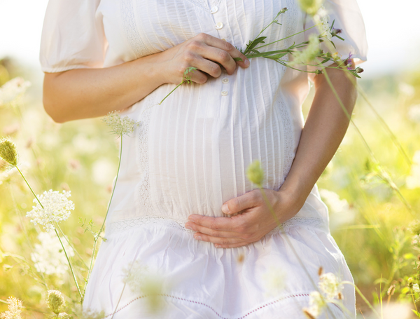Pregnant woman in a white dress holding wildflowers against her belly