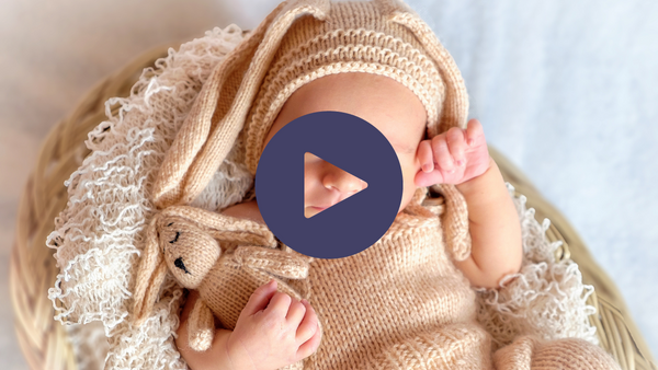 Video thumbnail of a sleeping newborn baby wearing a knitted bunny hat and holding a knitted bunny toy