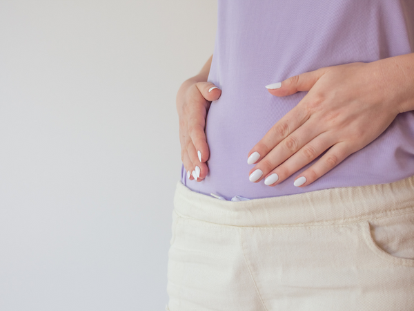 Close-up of a pregnant woman in a lilac top with her hands resting on her belly