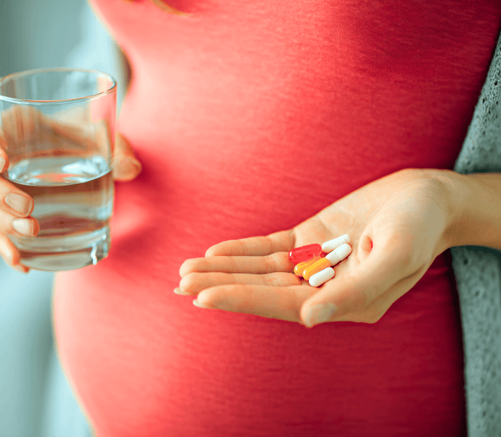 Close-up of a pregnant woman's belly in red holding a handful of supplement capsules and a glass of water