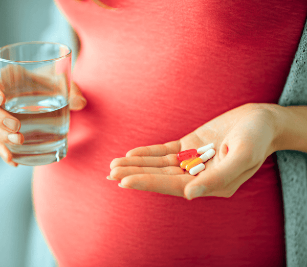 Close-up of a pregnant woman's belly in red holding a handful of supplement capsules and a glass of water
