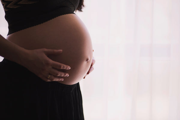 Close-up of a pregnant woman's bare belly with her hand resting on it, backlit by a bright window
