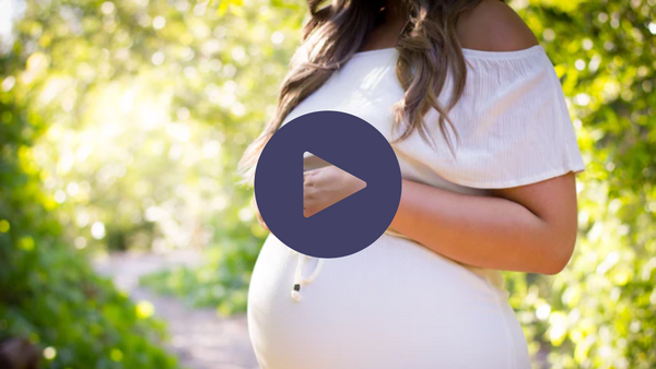 Pregnant woman outdoors in a white dress holding her belly