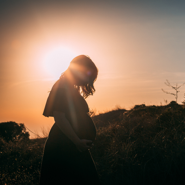 Silhouette of a pregnant woman standing in a field at sunset holding her belly