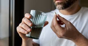 Man holding a glass of water and a supplement capsule