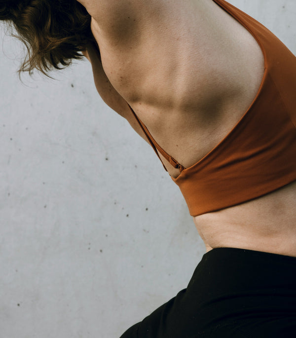Close-up of a woman's bare torso in an orange bralette, seen from the side