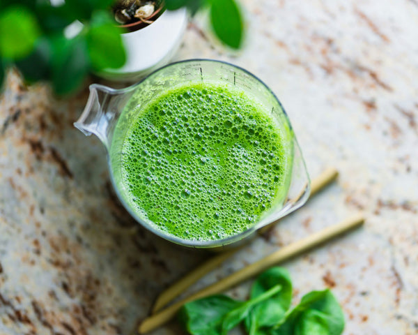 Overhead view of a green smoothie in a glass jug with straws and spinach leaves nearby