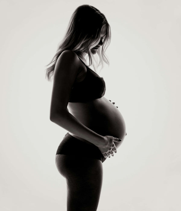 Black and white silhouette of a pregnant woman in underwear cradling her bare belly