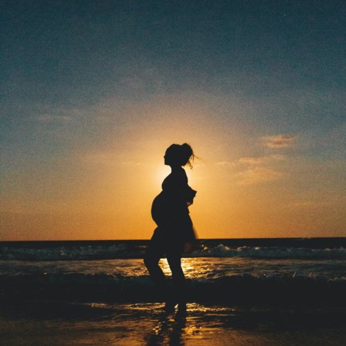 Silhouette of a pregnant woman standing on a beach at sunset