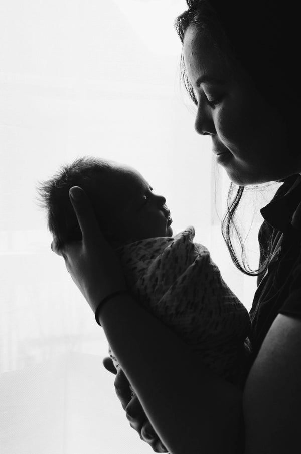 Silhouette of a mother gently holding her newborn baby up to her face by a window