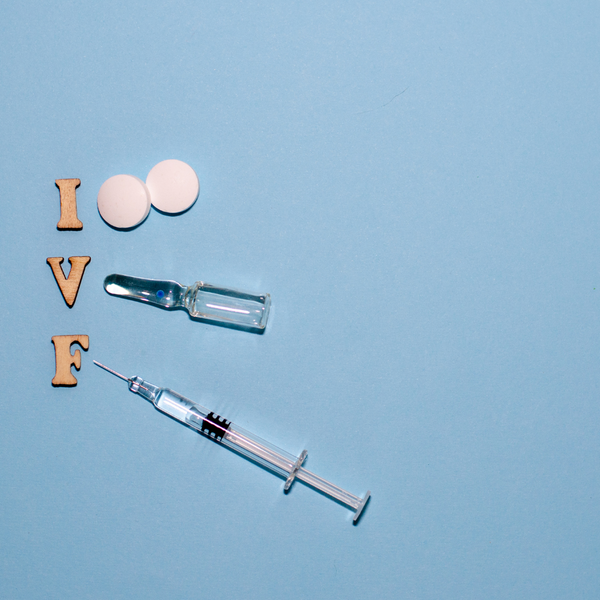 Wooden letters spelling IVF beside pills, a vial and a syringe on a blue background