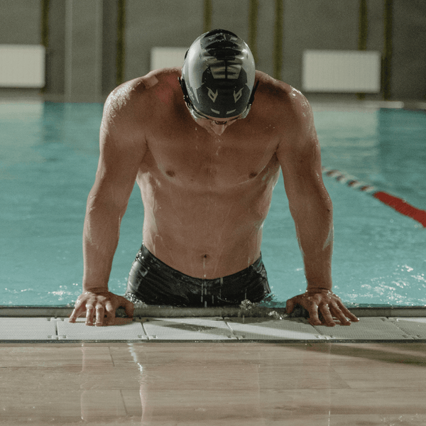 Swimmer wearing a cap and goggles emerging from a pool
