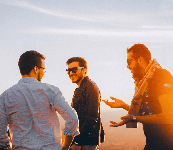 Three young men laughing and talking together outdoors at sunset