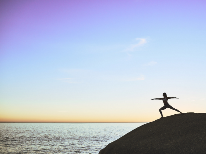 Silhouette of a woman doing a yoga pose on a cliff overlooking the ocean at sunset