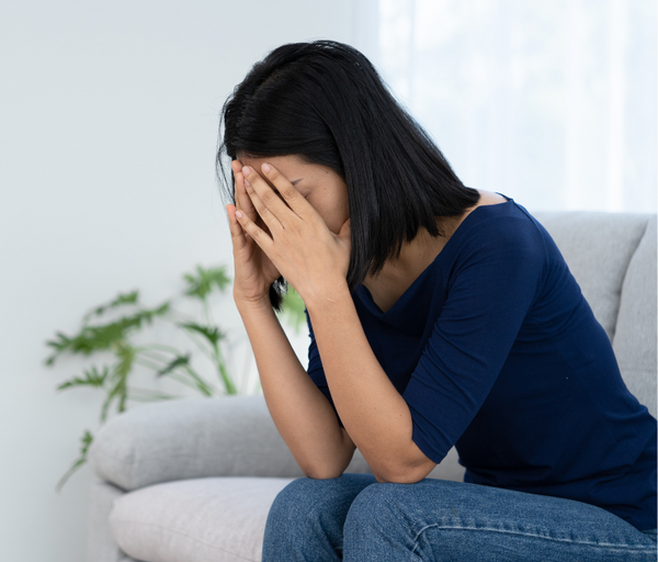 Woman sitting on a sofa with her face in her hands looking upset