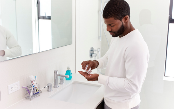 Man pouring a supplement capsule into his hand in a bathroom