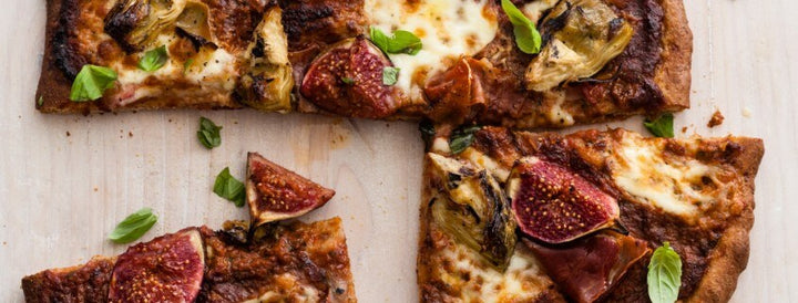 Sliced flatbread pizza topped with figs, prosciutto, cheese and basil leaves