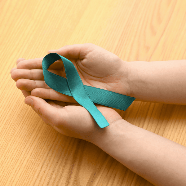 Hands cupping a teal awareness ribbon on a wooden table