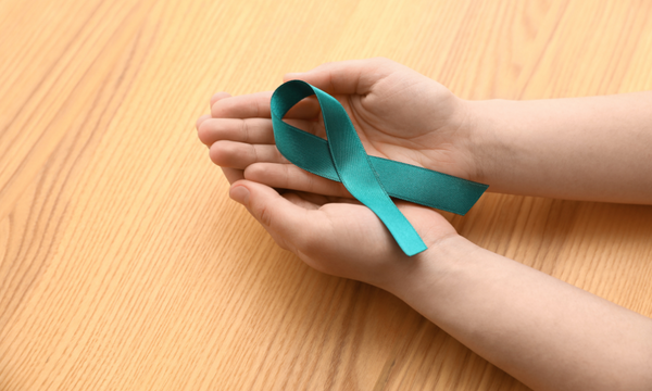 Hands holding a teal awareness ribbon on a wooden table