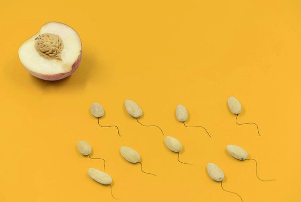 Halved peach beside almond shapes with drawn tails resembling sperm on a yellow background