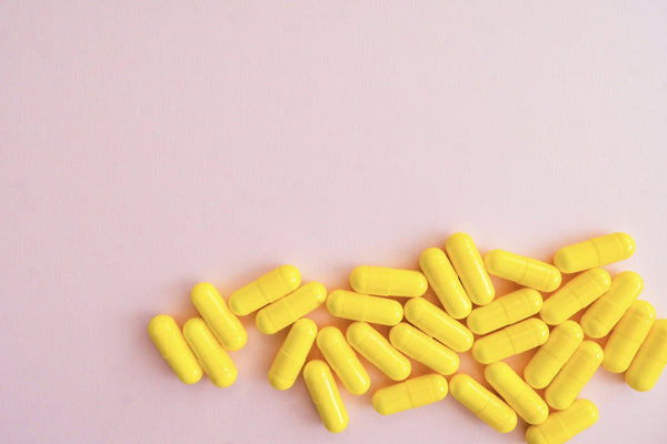 Yellow supplement capsules scattered on a pink background