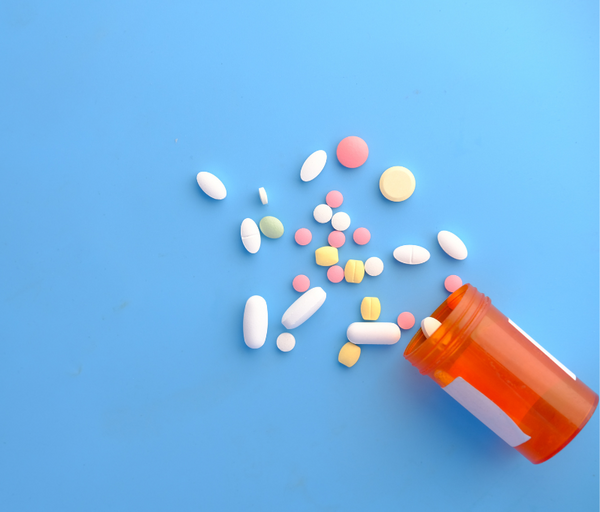 Assorted colourful pills and capsules spilled from an orange prescription bottle