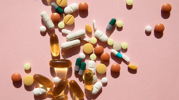 Assorted vitamin and supplement pills and capsules scattered on a pink background