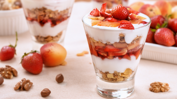 Glasses layered with yogurt, granola, strawberries and stone fruit, garnished with nuts