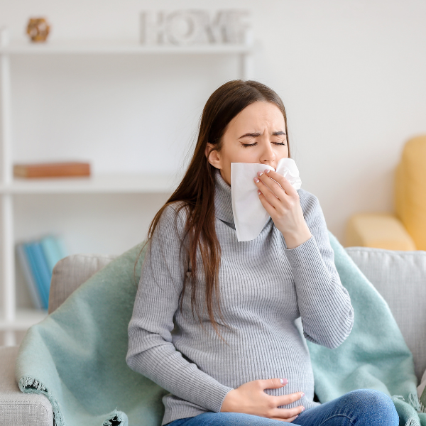 Pregnant woman sitting on a sofa blowing her nose into a tissue