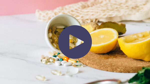 Bowl of supplement capsules spilled next to halved lemons on a marble surface