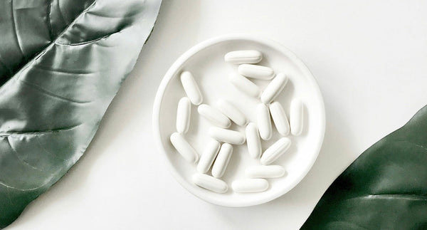 White supplement capsules in a small dish beside two large leaves