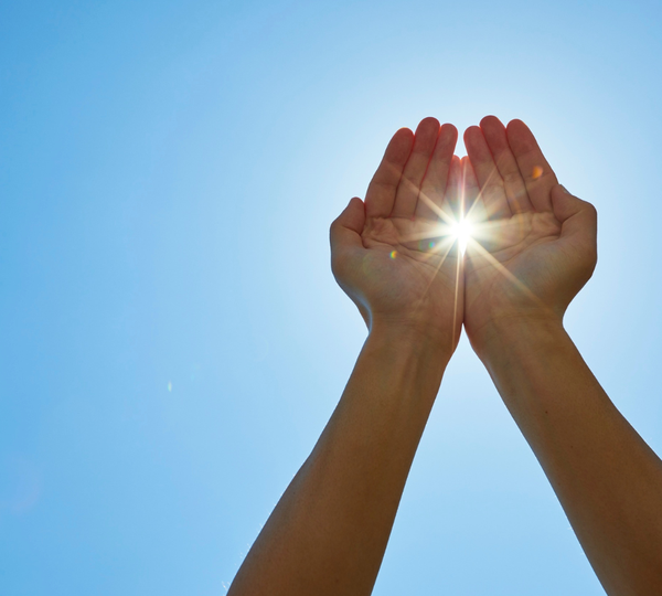 Two cupped hands raised toward a bright sun in a blue sky