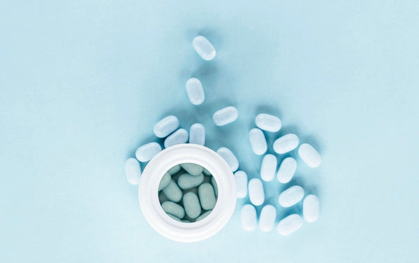 White pills spilling out of an open bottle on a blue background