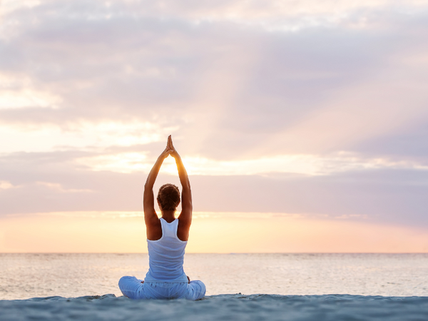 Woman practicing yoga on a beach at sunset with hands raised overhead