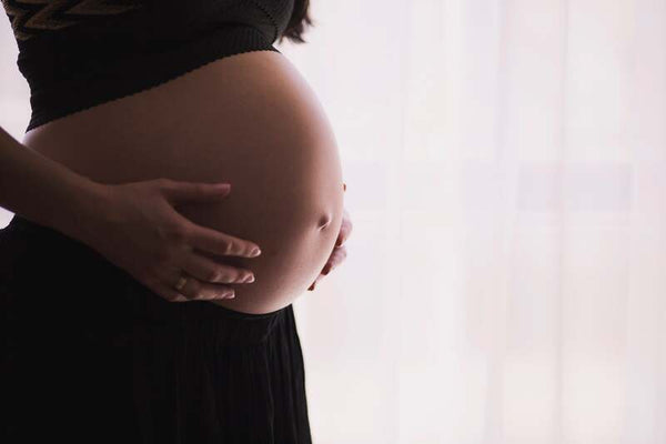 Close-up of a pregnant woman's bare belly with her hand resting on it, backlit by a bright window