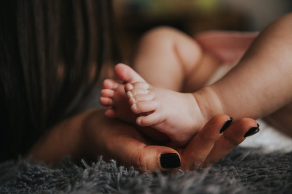 Adult hand holding a baby's feet on a fuzzy grey blanket