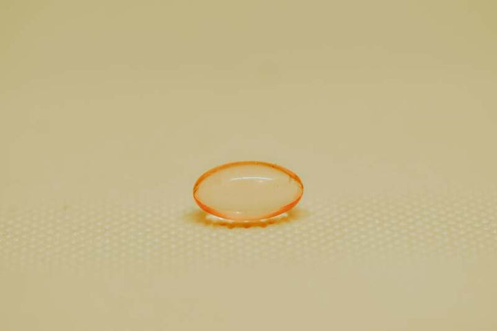 Single orange vitamin E softgel capsule on a light textured surface