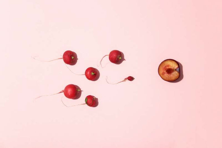 Radishes and a halved plum arranged on a pink background