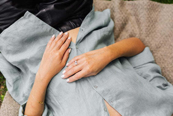 Hands with white-painted nails resting on a sage green linen dress, one wearing a delicate ring