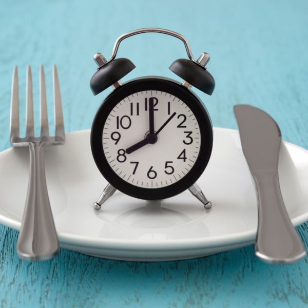 Black alarm clock on a white plate with a fork and knife on a blue wooden surface