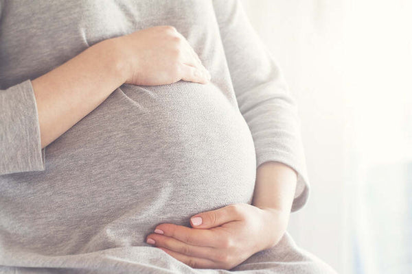 Pregnant woman in a grey top cradling her baby bump with both hands