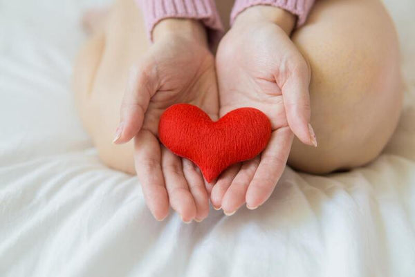 Hands cupping a small red heart-shaped cushion against a white background