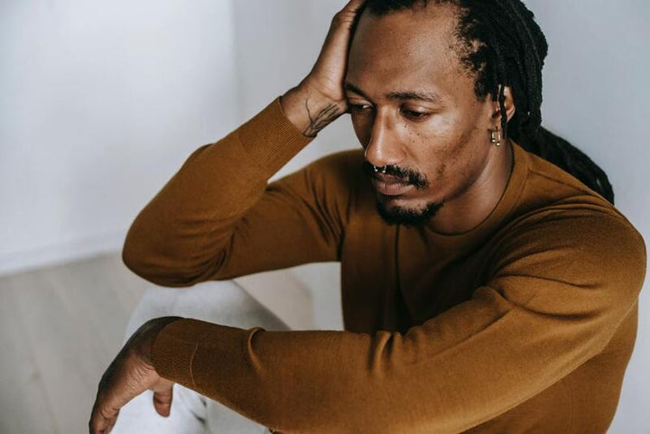 Man sitting with his hand on his head, looking down pensively