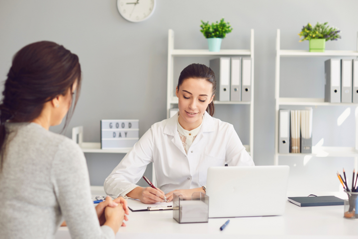 Doctor writing on a clipboard while talking with a patient in an office