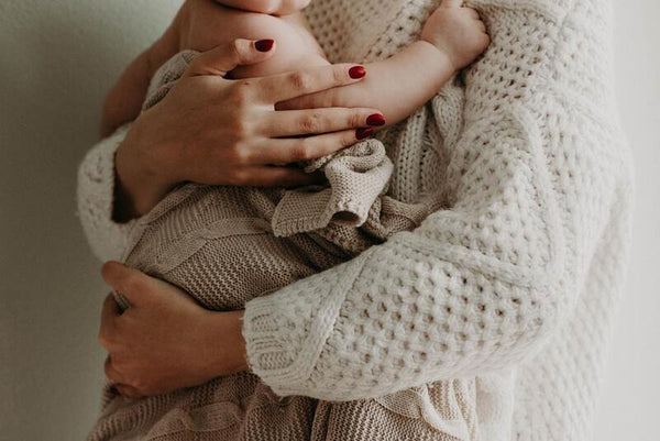 Woman cradling a baby wrapped in a chunky cream knit blanket