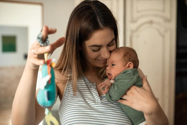 Woman kissing her newborn baby's head while holding a colourful toy