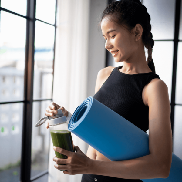 Woman in workout clothes holding a blue yoga mat and a green juice bottle