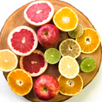 Sliced citrus fruits and whole red apples arranged on a round wooden board