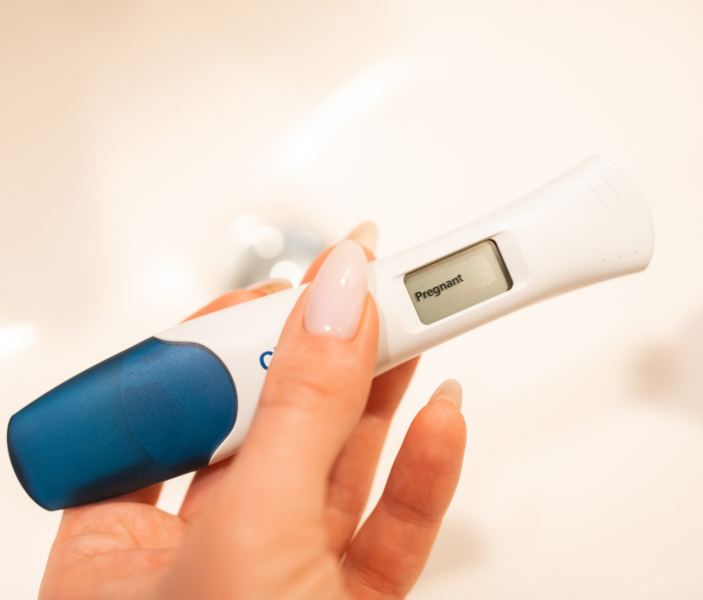 Digital pregnancy test displaying 'Pregnant' held in a hand with pink nails
